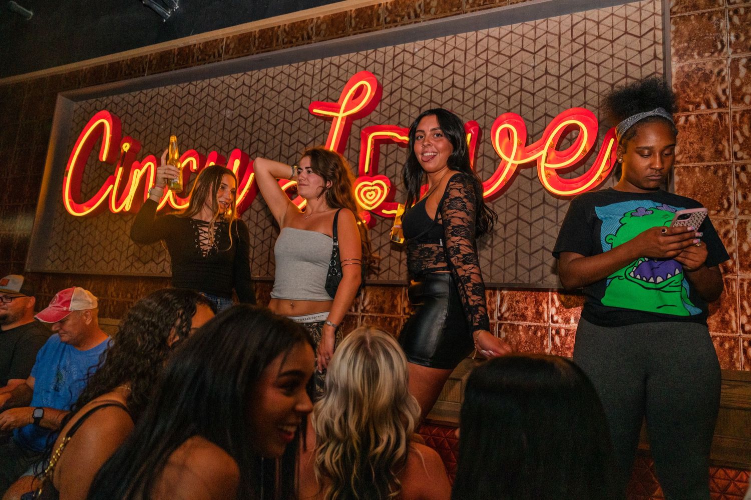 Women socializing and dancing under the Cincinnati Love neon sign at a nightclub.