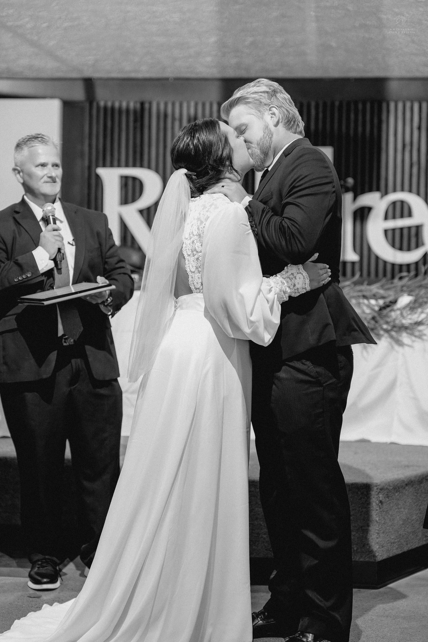 Bride and groom share their first kiss at the altar during a wedding ceremony in black and white.