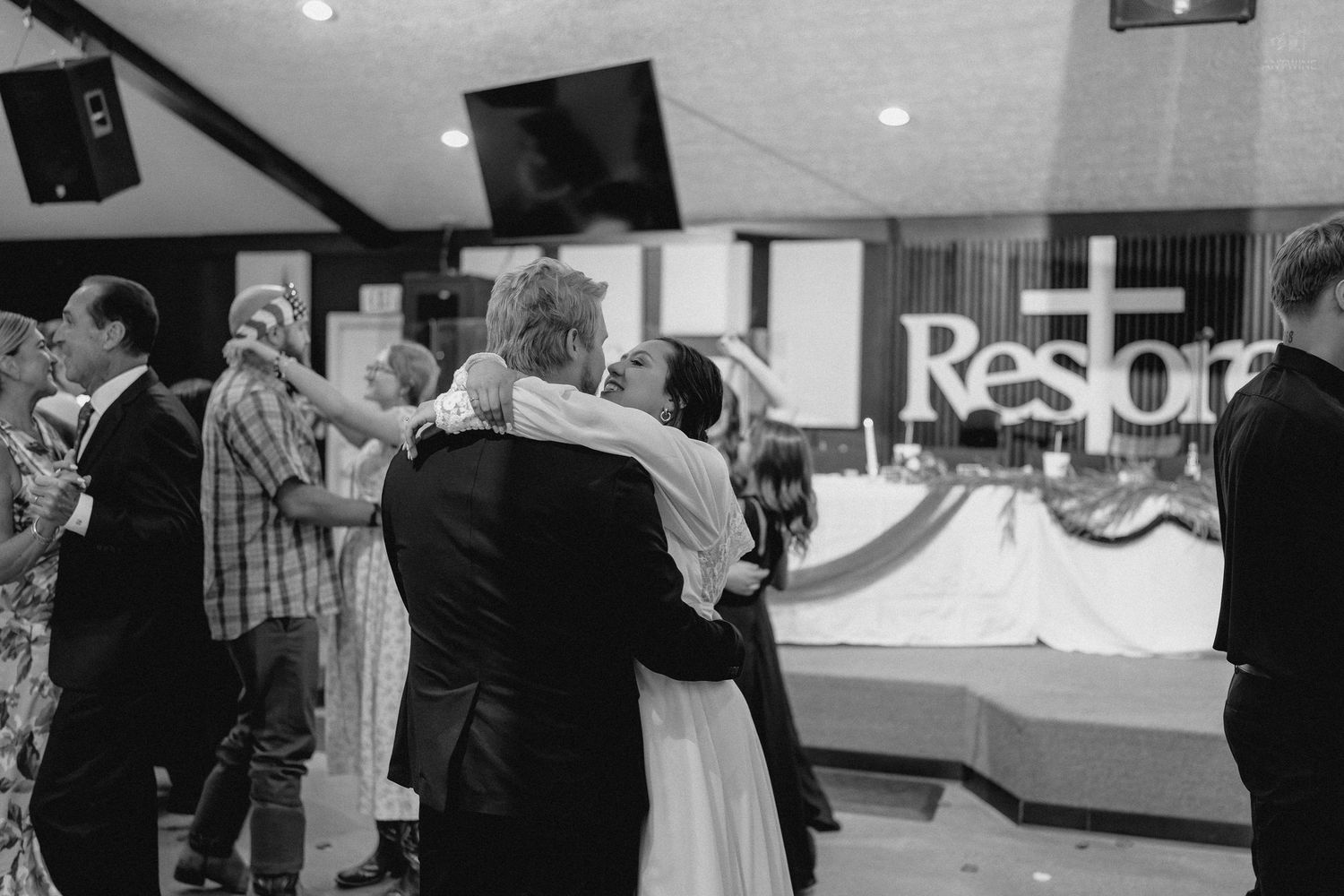 Black and white photo of couple embracing on dance floor at church wedding reception.