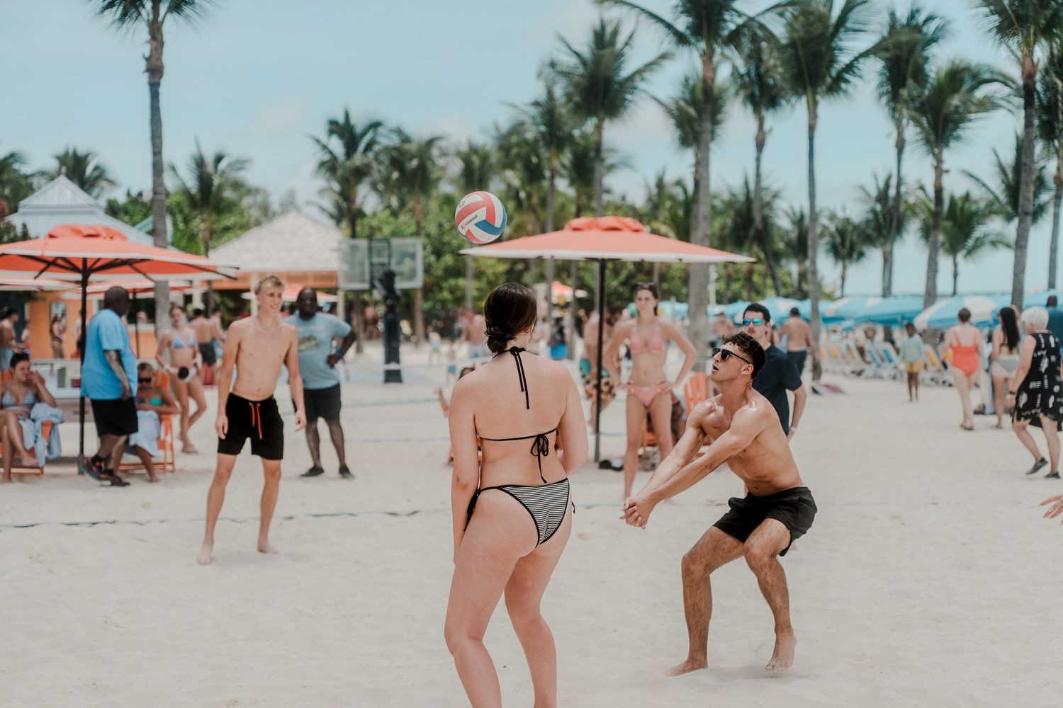 Beach volleyball players bumping the ball on a sunny tropical sandy court.