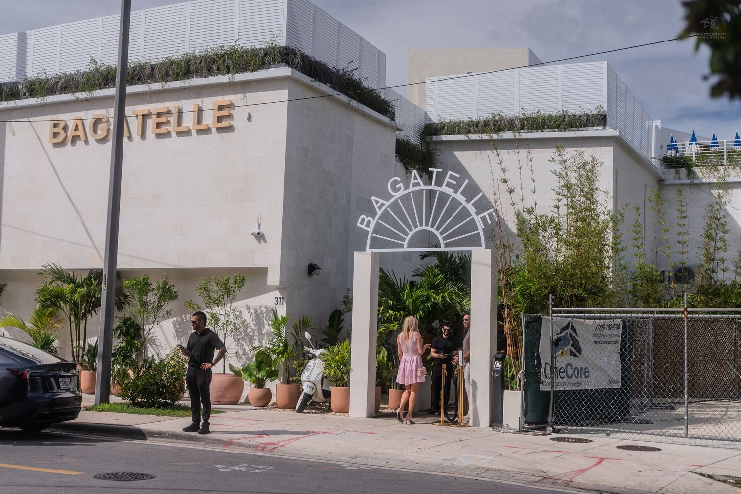 People gather outside the Bagatelle restaurant entrance on a sunny Miami street.