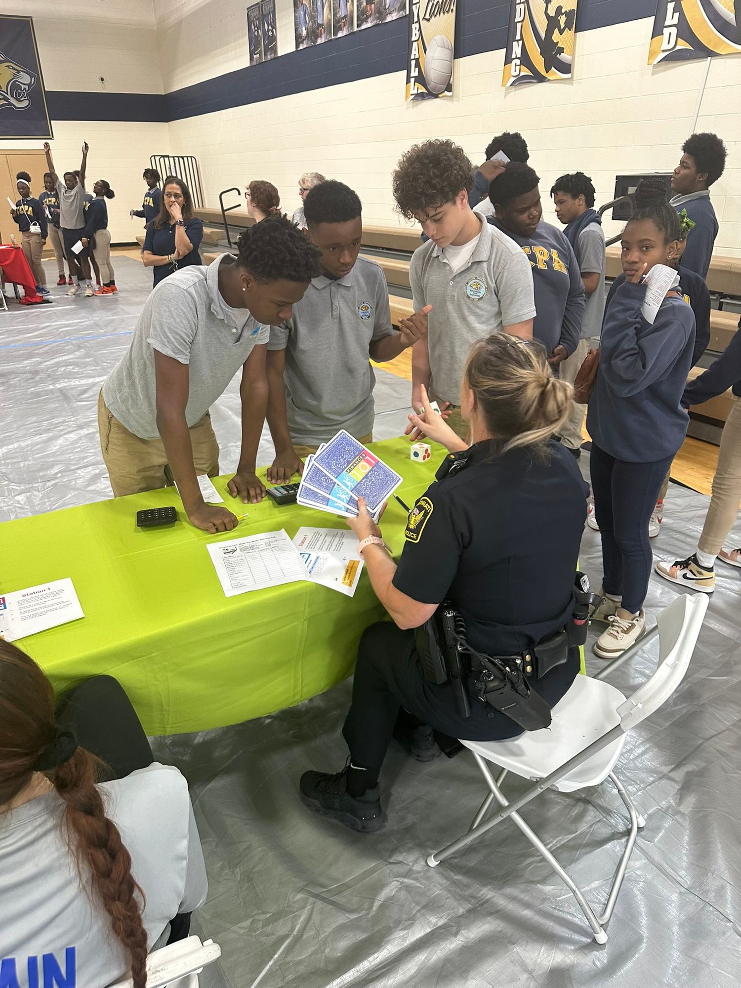 A police officer shares informational brochures with students at a school career fair event.