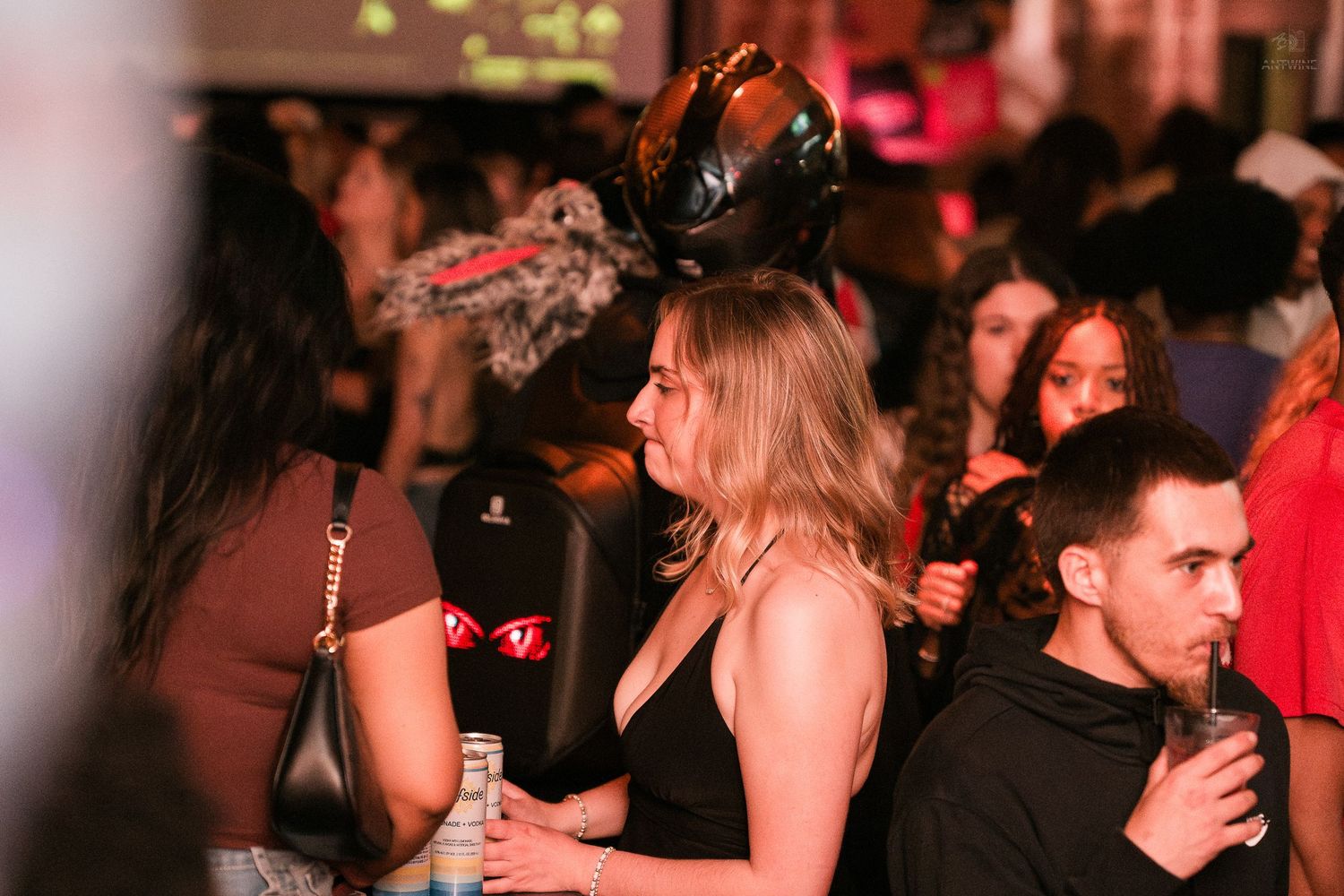 Woman wearing decorative black headpiece stands out in a crowded nightclub holding an inflatable.
