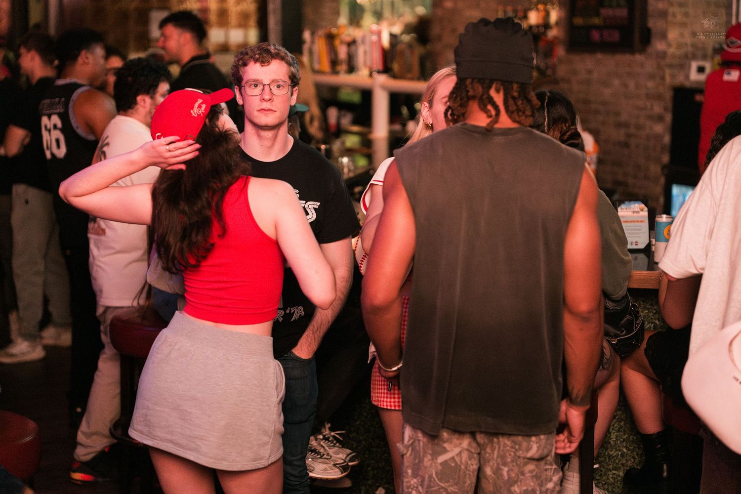 Young adults socializing and dancing in a dimly lit bar with red ambient lighting.