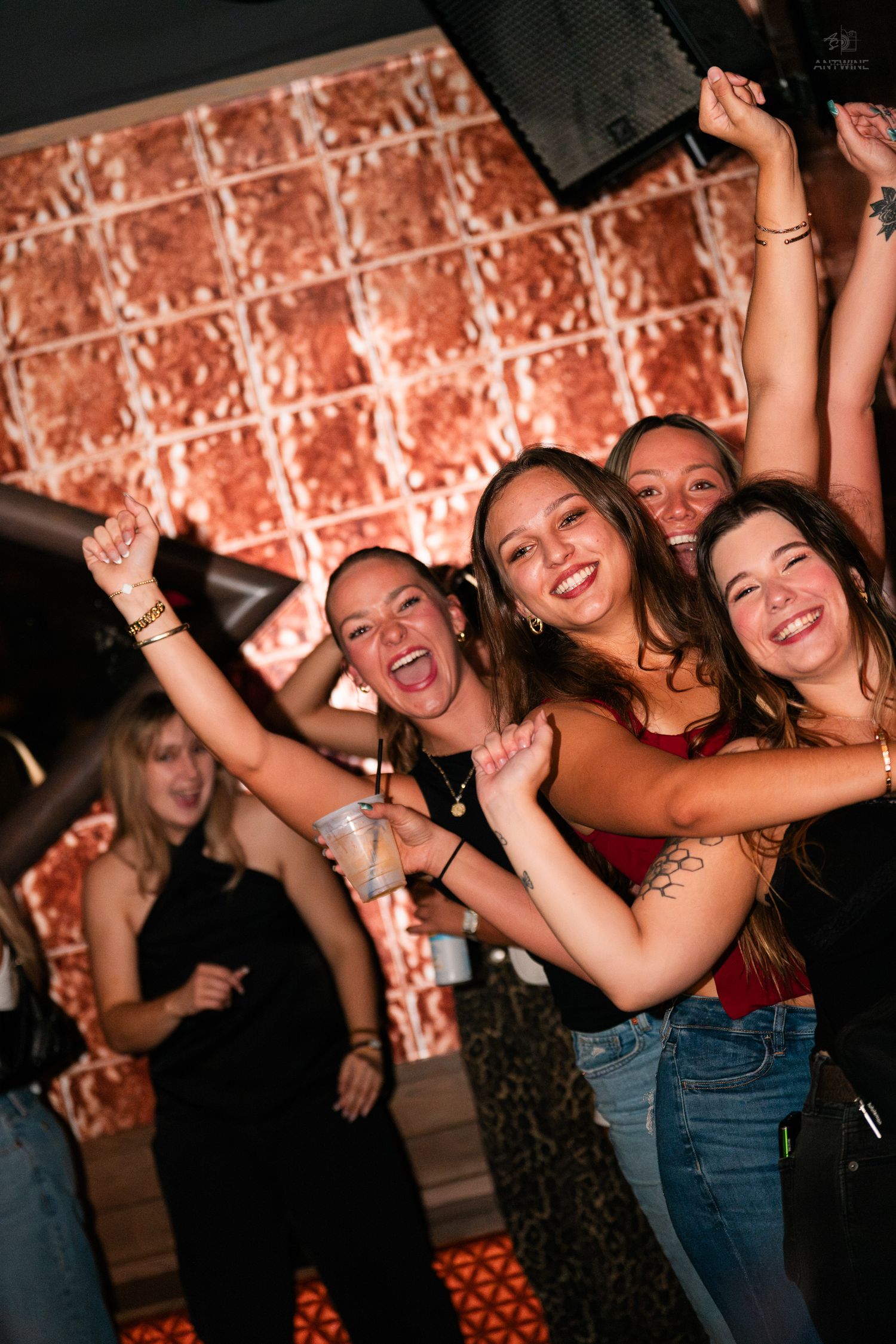 Group of smiling women dancing and celebrating with raised arms at a nightclub.