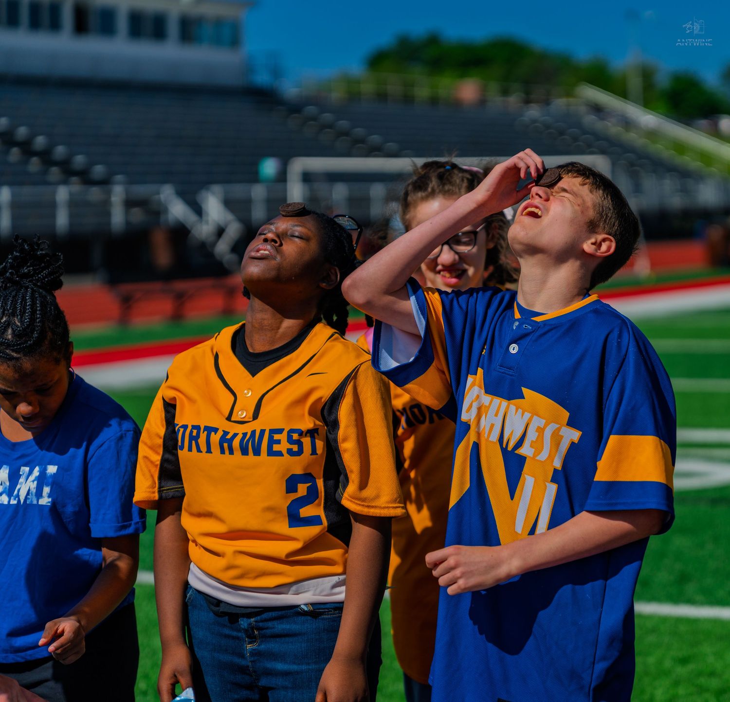Kids in Northwest jerseys laugh and look up on a sunny football field.
