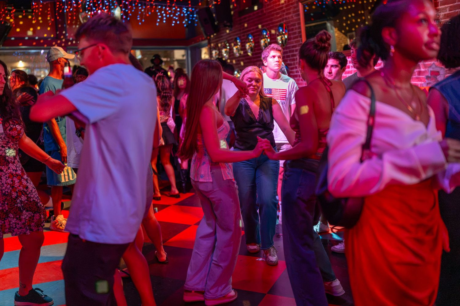 Diverse group of people socializing and dancing at a festive indoor party with red ambient lighting.