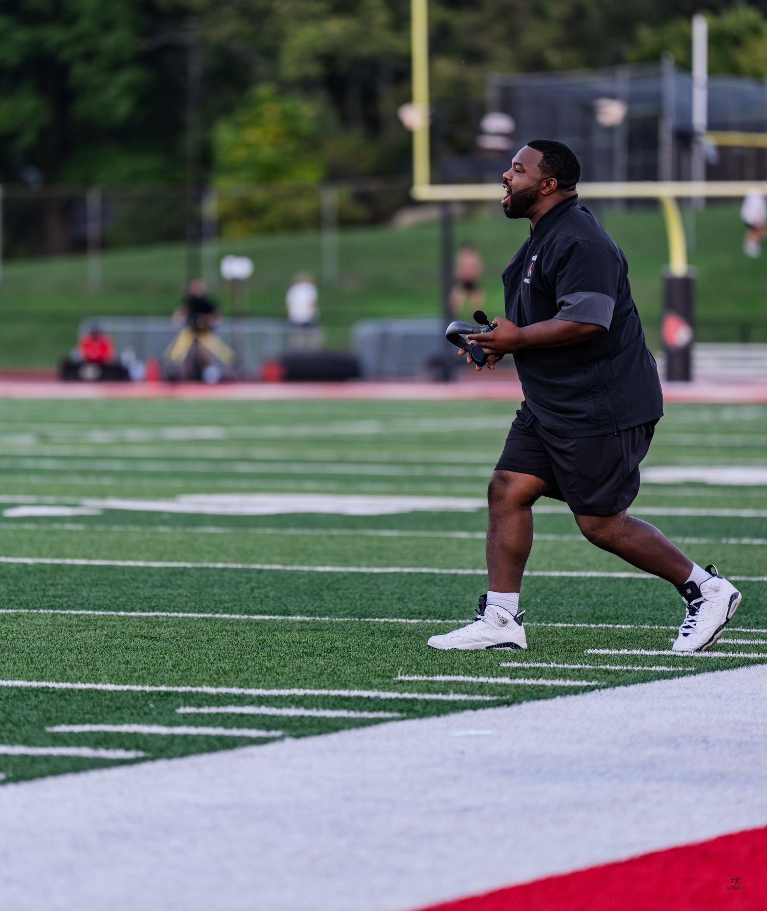 A football coach in black shorts runs along the sideline during a high school football game.