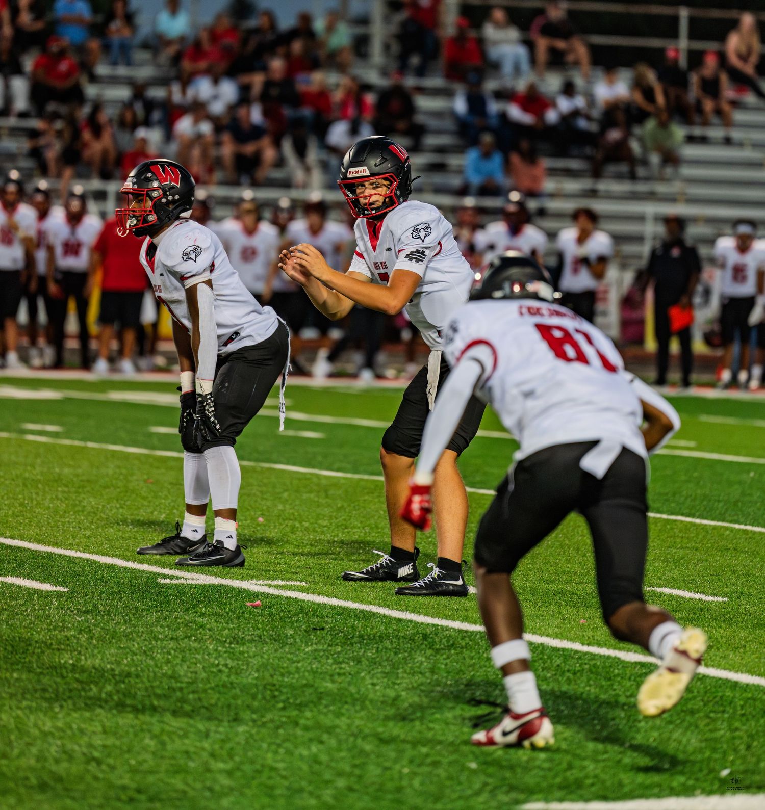 High school football quarterback in white uniform prepares to snap the ball during a competitive game.
