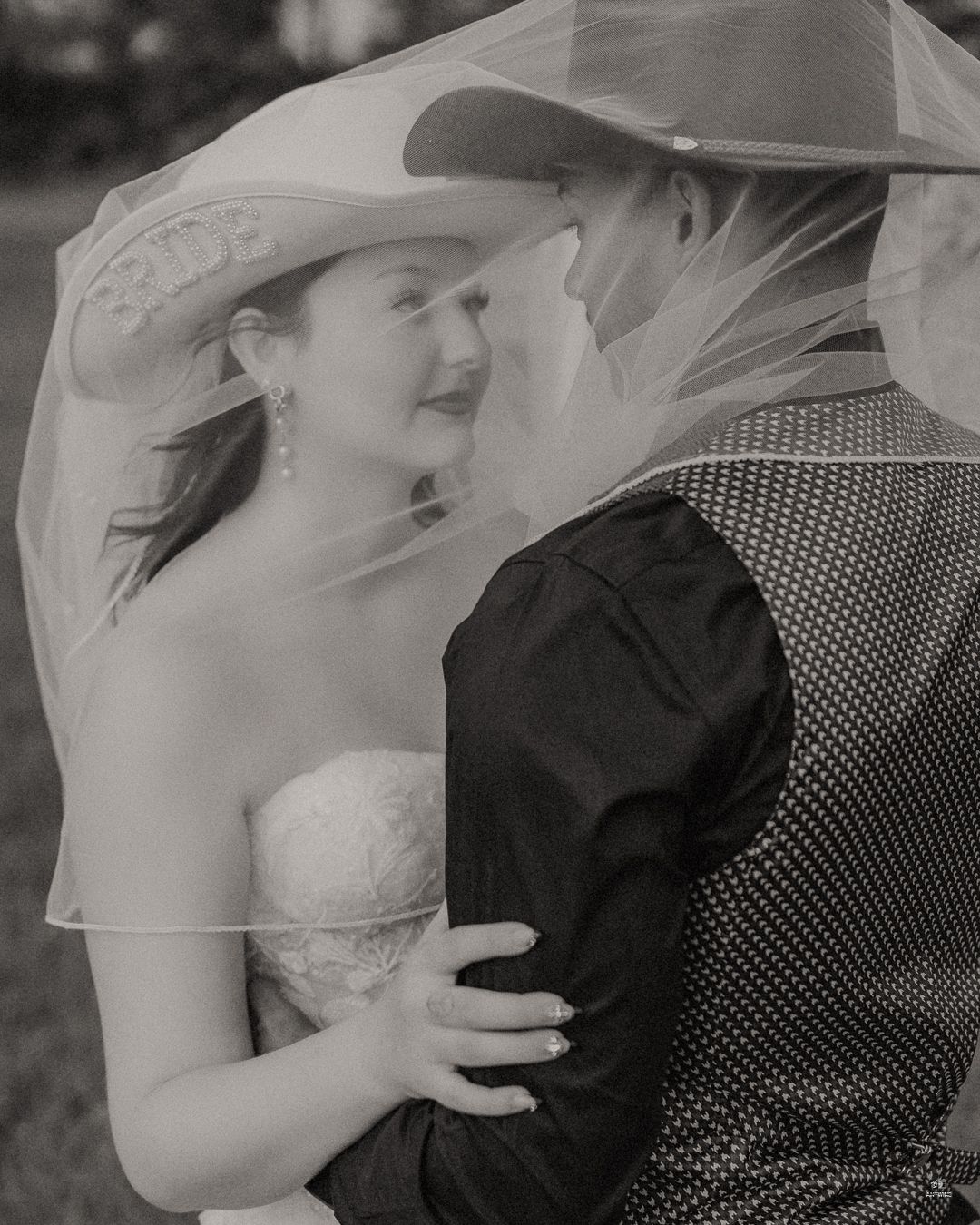 Black and white romantic photo of bride and groom sharing intimate moment under wedding veil.