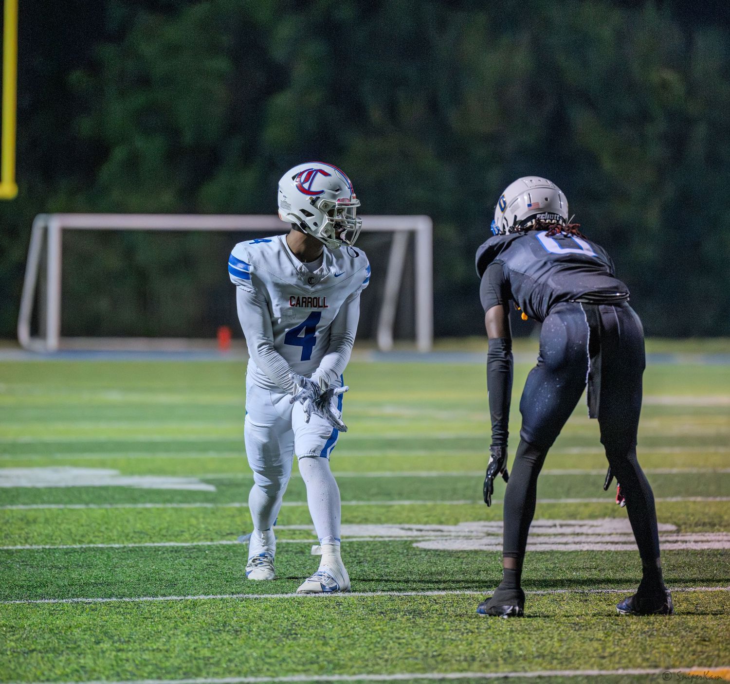 Two high school football players face off at the line of scrimmage during an evening football game.