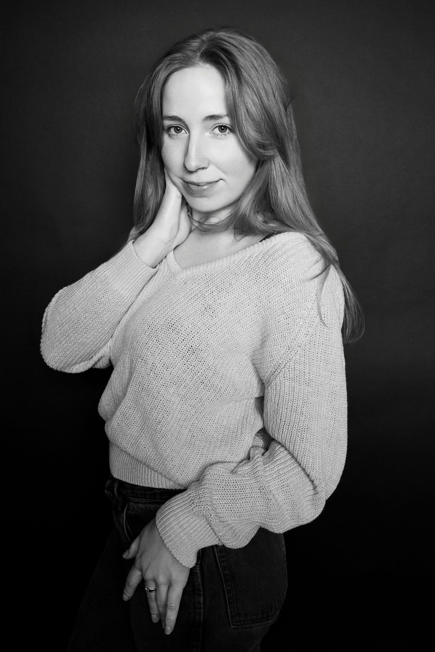 Black and white studio portrait of a woman in a knit sweater, hand resting gently against her cheek.