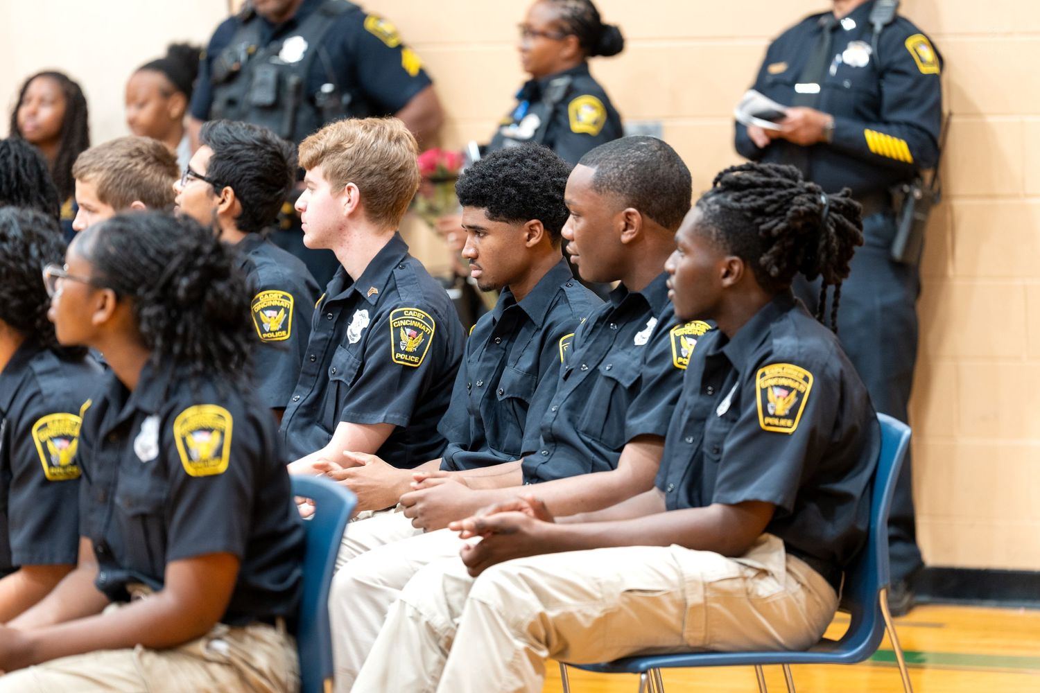 Young cadets in black uniforms with sheriff badges sit in rows during a law enforcement youth program ceremony in a gymnasium.