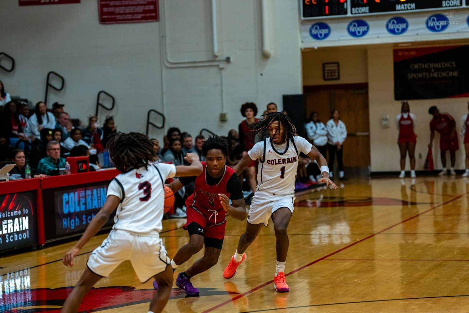 Colerain Cardinals players defend opponent in red during intense high school basketball game.