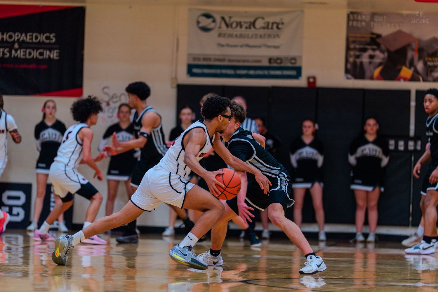 Female basketball players compete for ball possession during an intense high school game in a gymnasium.
