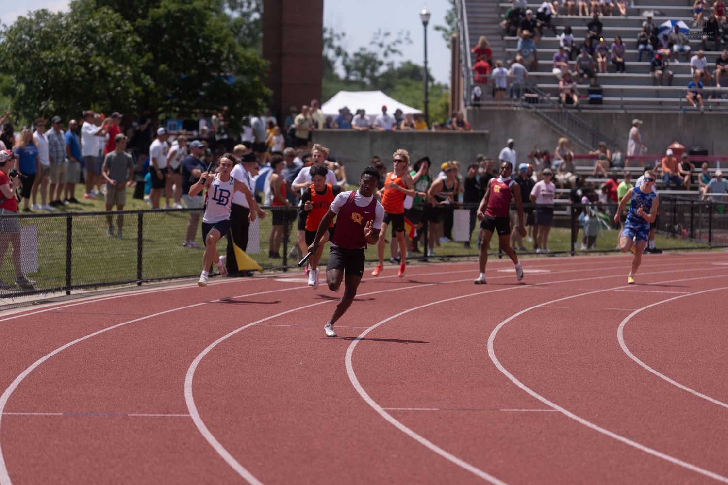 Young runners compete in a sprint race on a red track at a sunny outdoor athletic competition.