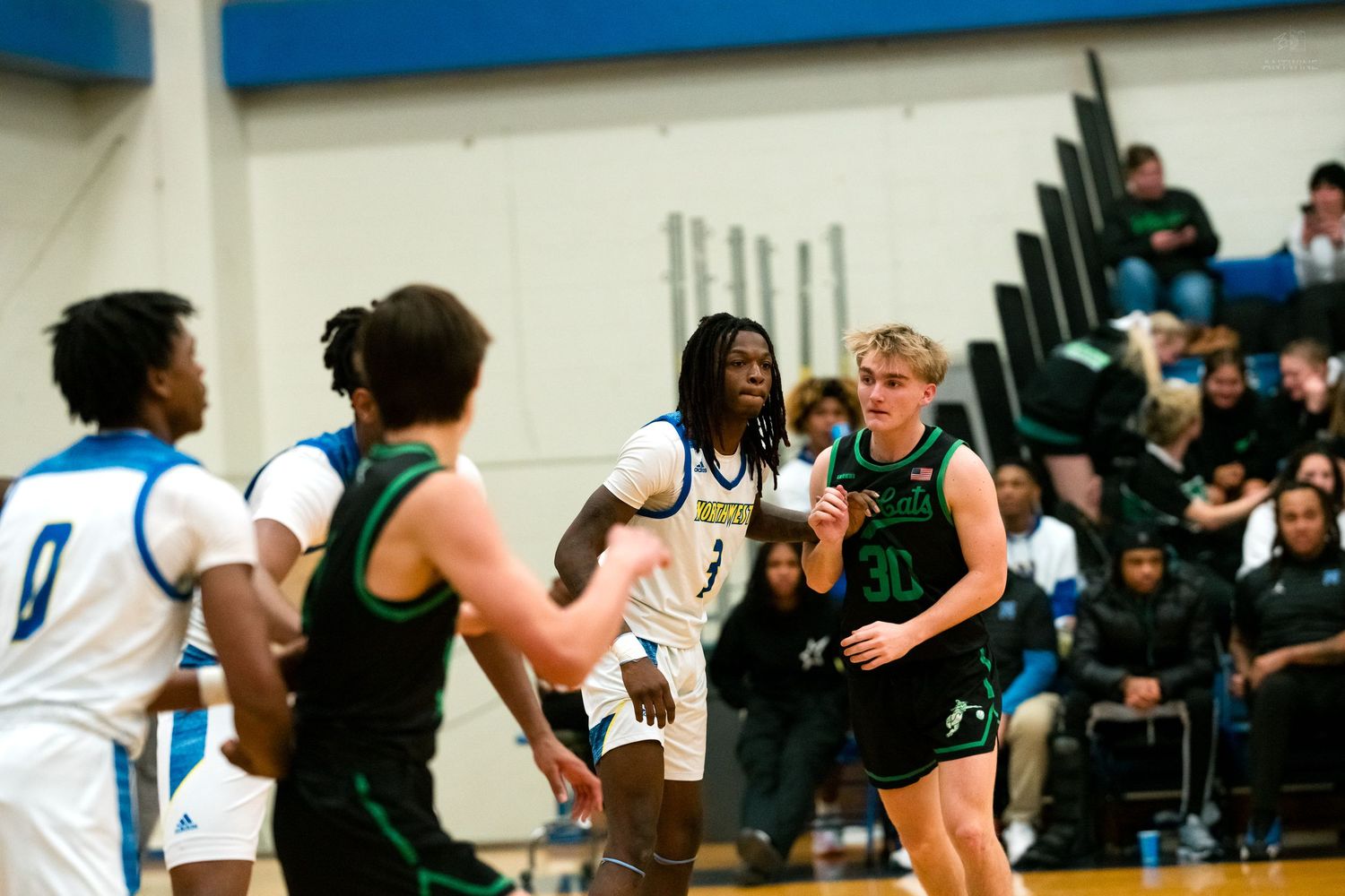 High school basketball players in green and white uniforms compete for position near the key during a game.