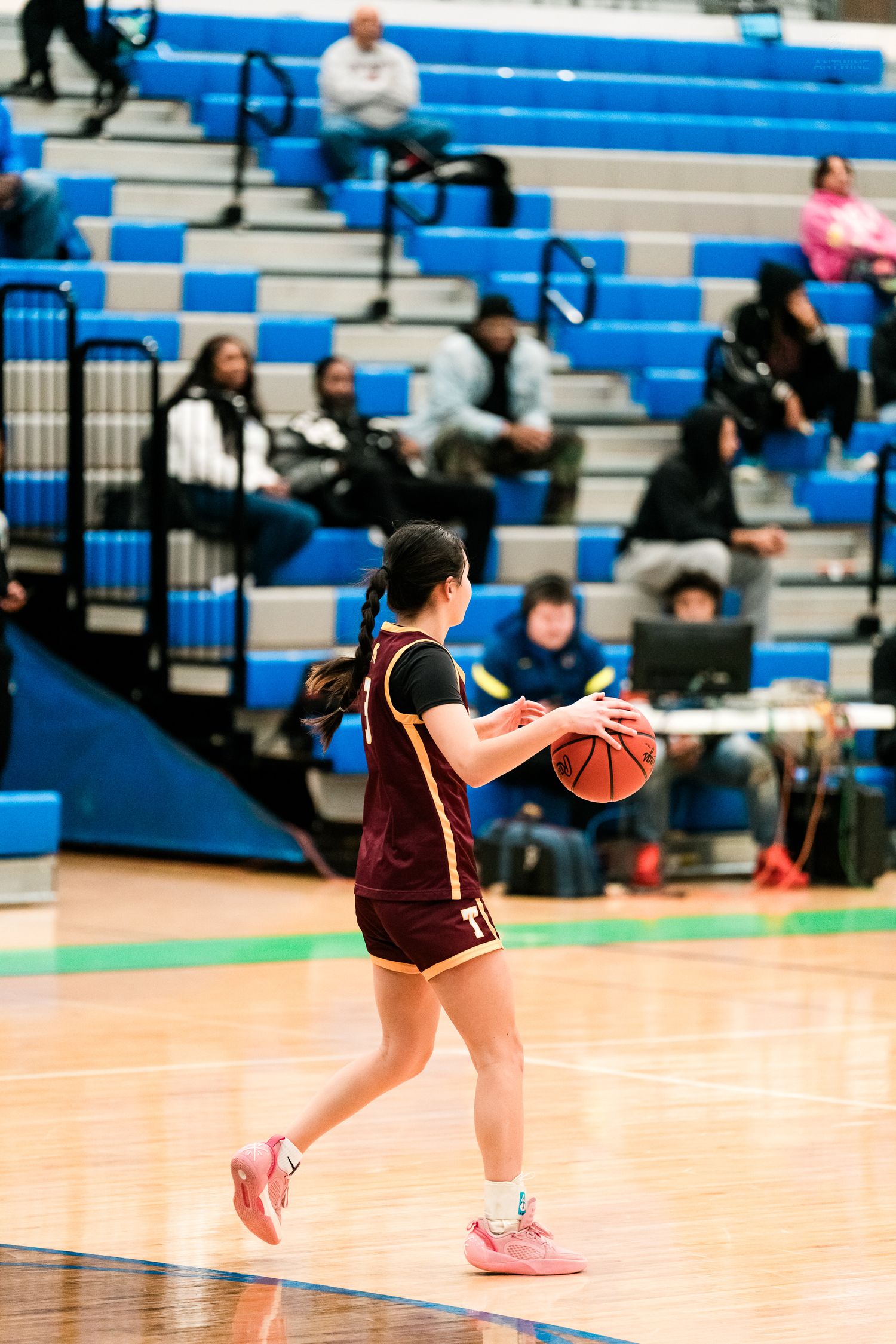 A female basketball player in maroon uniform dribbles the ball during a high school girls basketball game.