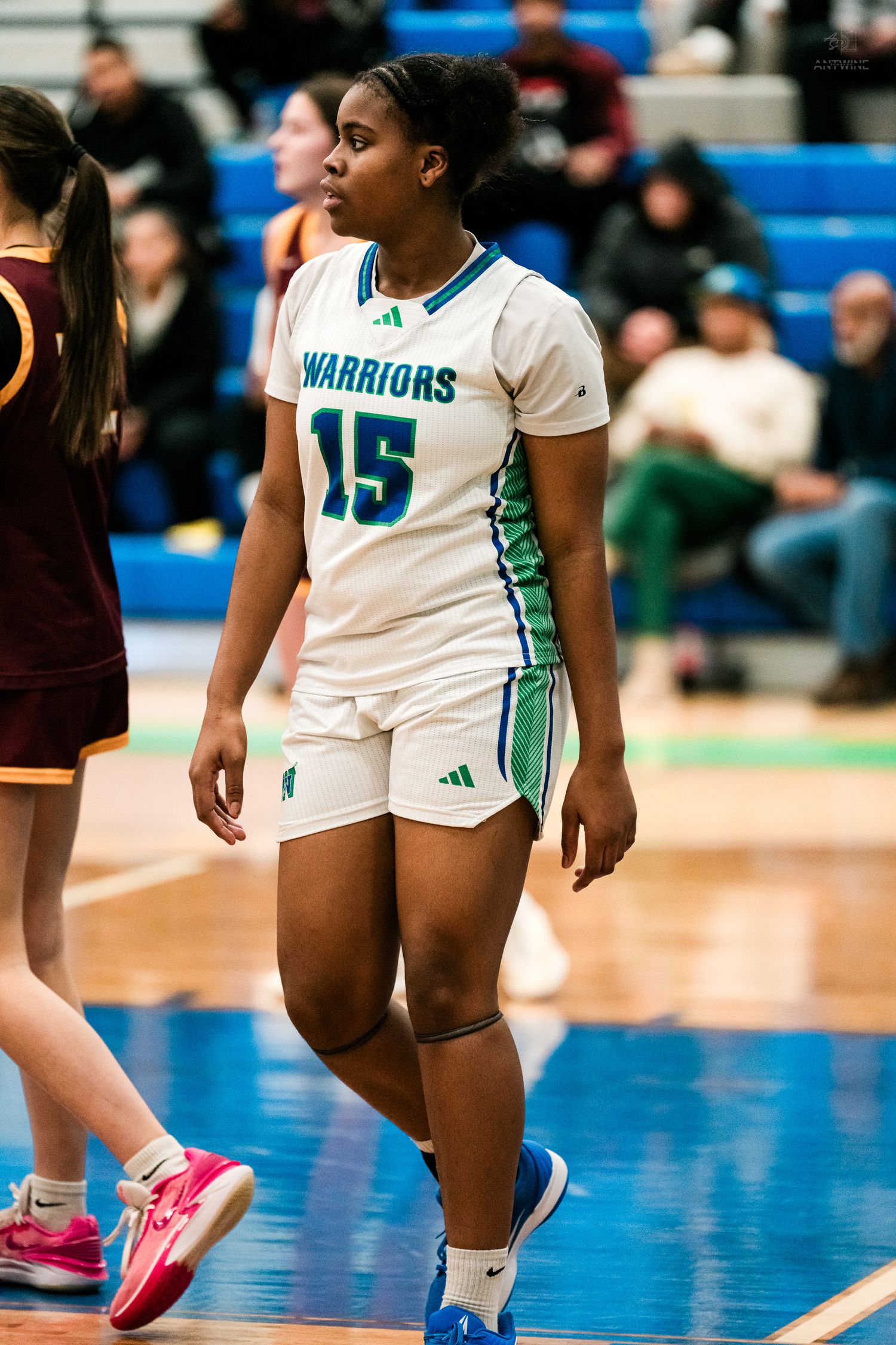 Warriors girls basketball player #15 walks on court in white and teal uniform during a high school game.
