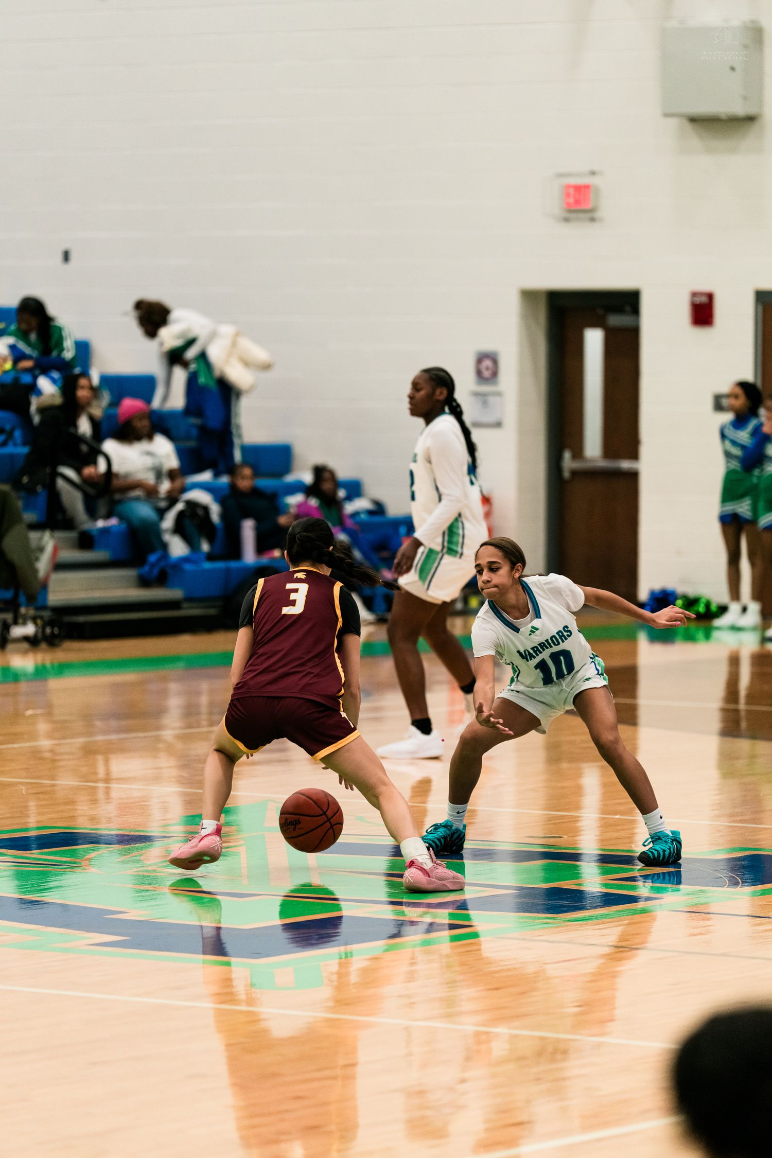 Player #3 dribbles the ball while defender #10 in white Warriors uniform plays defense in girls basketball game.
