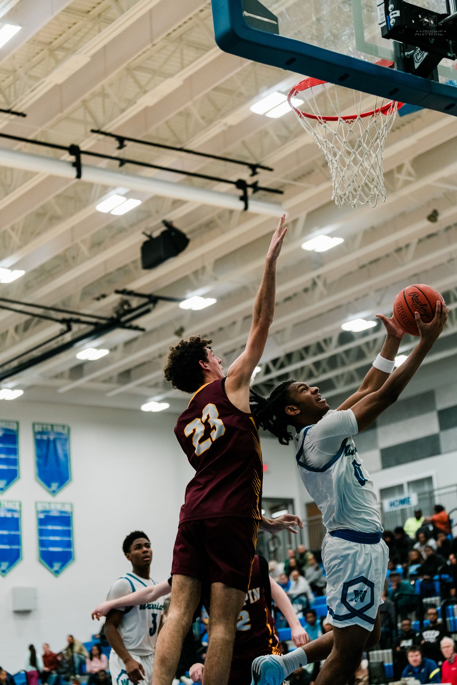 Player #23 in maroon Turpin jersey contests a layup attempt by a Warriors player in a high school basketball game.