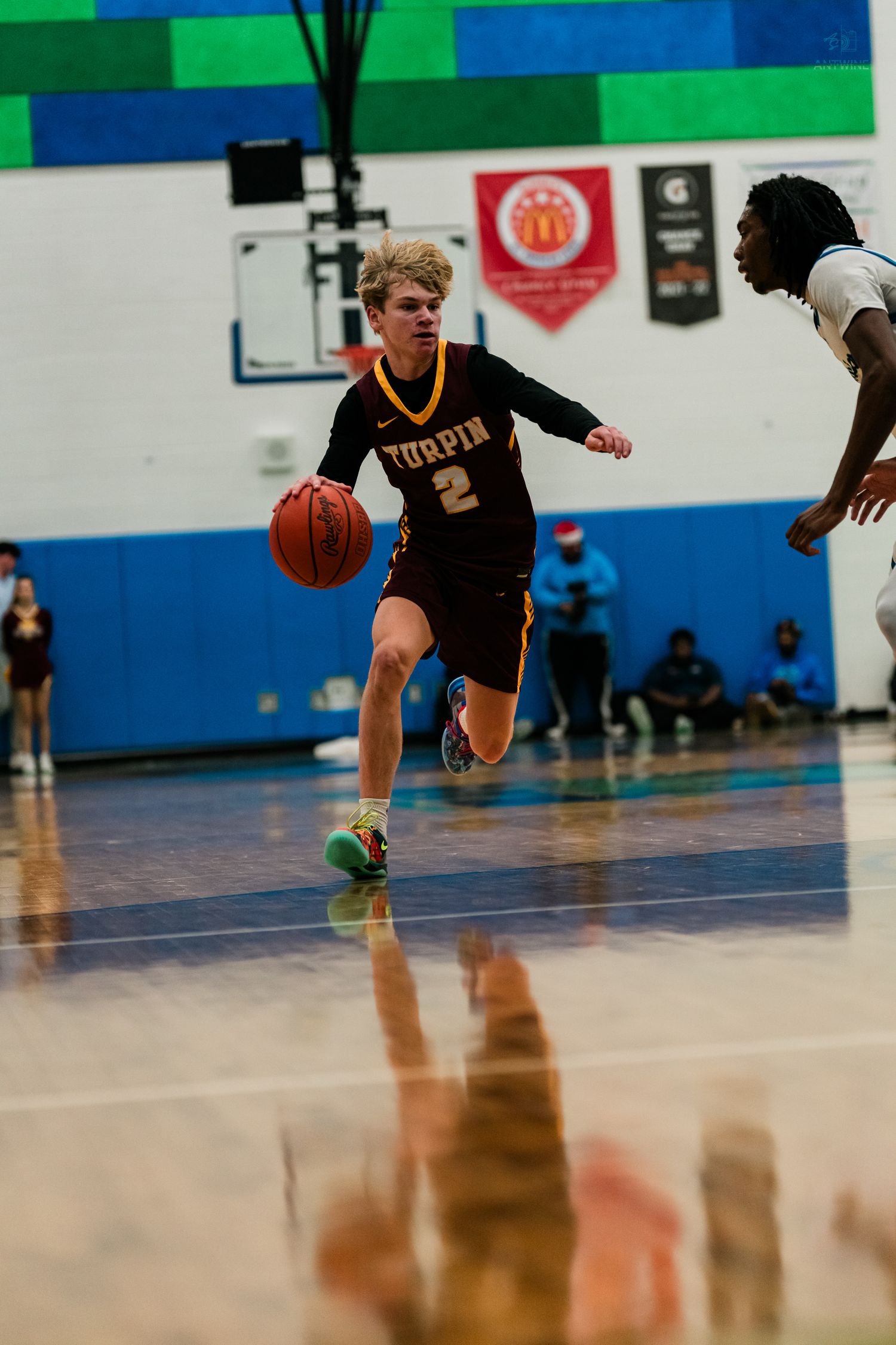 Turpin #2 drives baseline with ball during high school varsity basketball game in blue gymnasium.