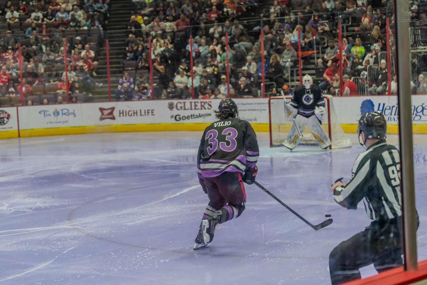 Hockey player number 33 in purple jersey skates on ice during a professional indoor hockey game.