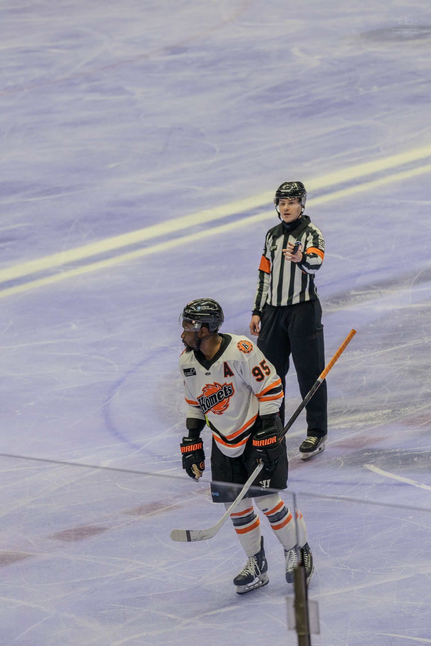Hockey referee signals a call while player number 95 in white and orange uniform skates nearby on ice.