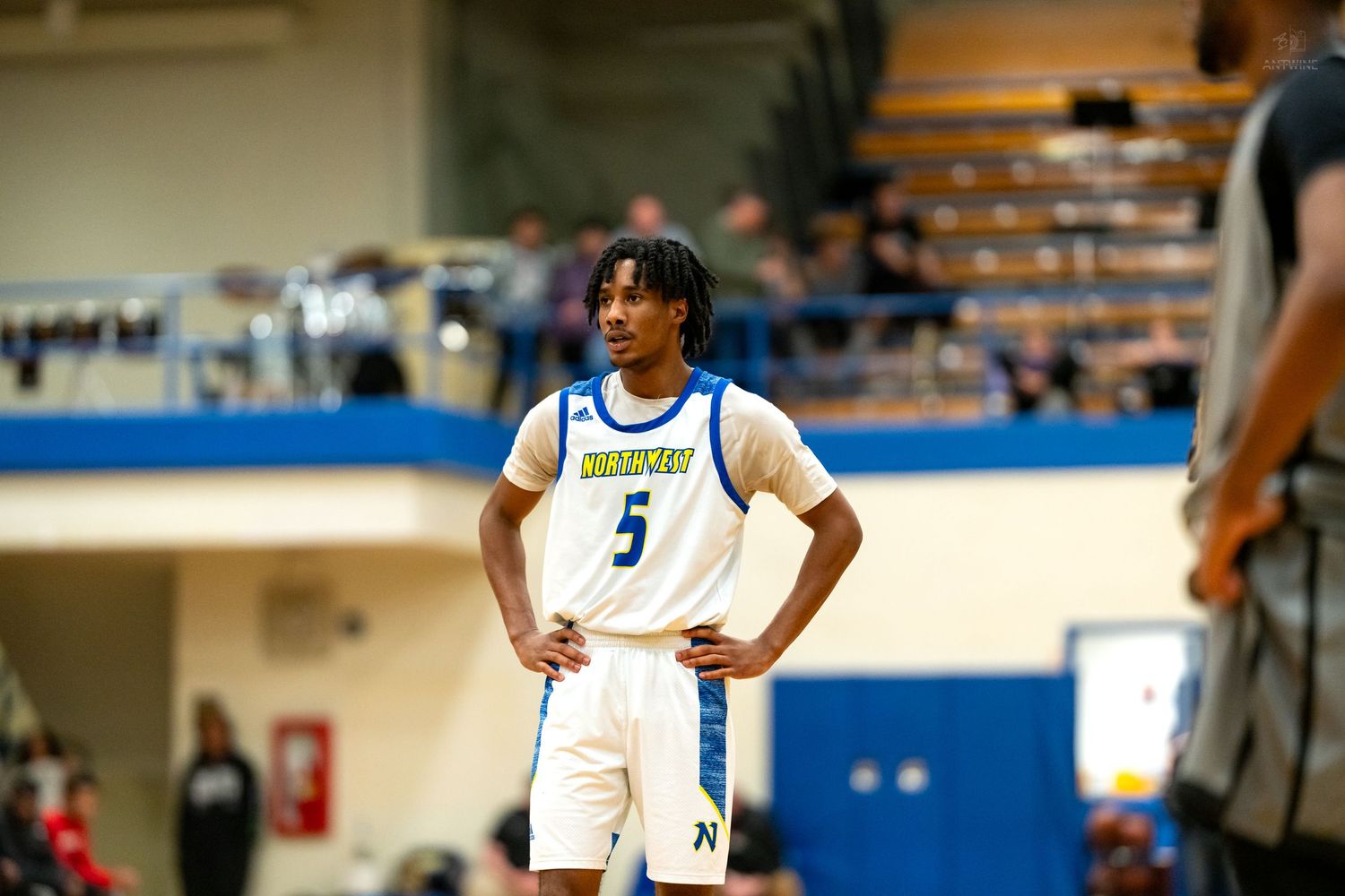 Player #5 in Warriors blue and white uniform stands with hands on hips during high school basketball game.