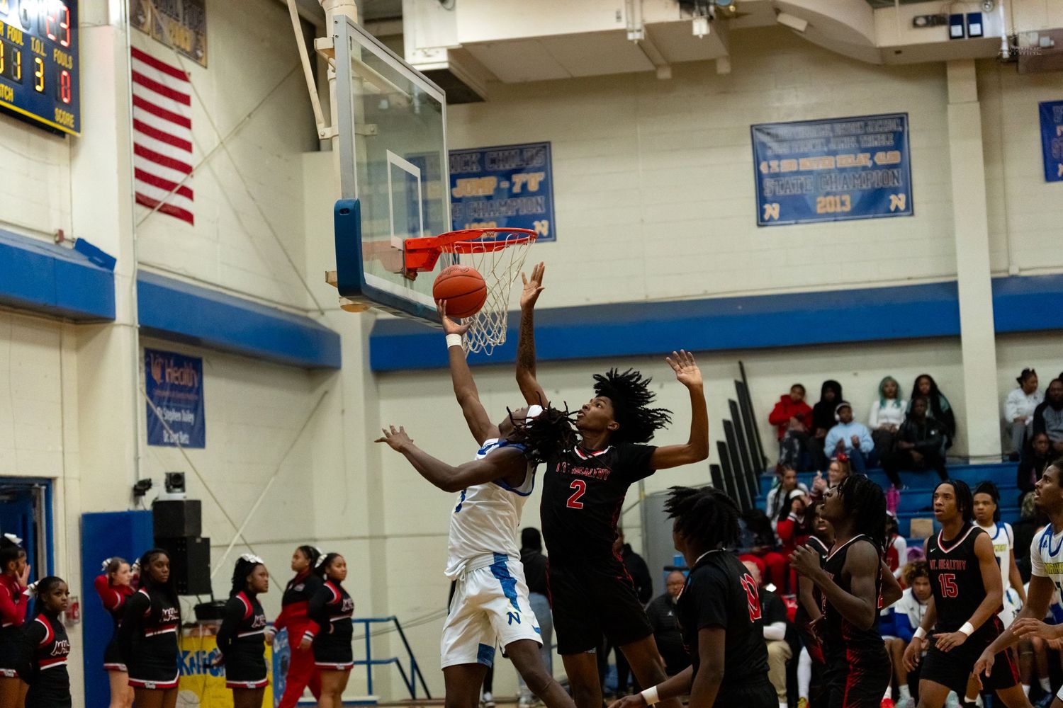 A basketball player in black number 2 jersey blocks a shot attempt during an intense high school basketball game.