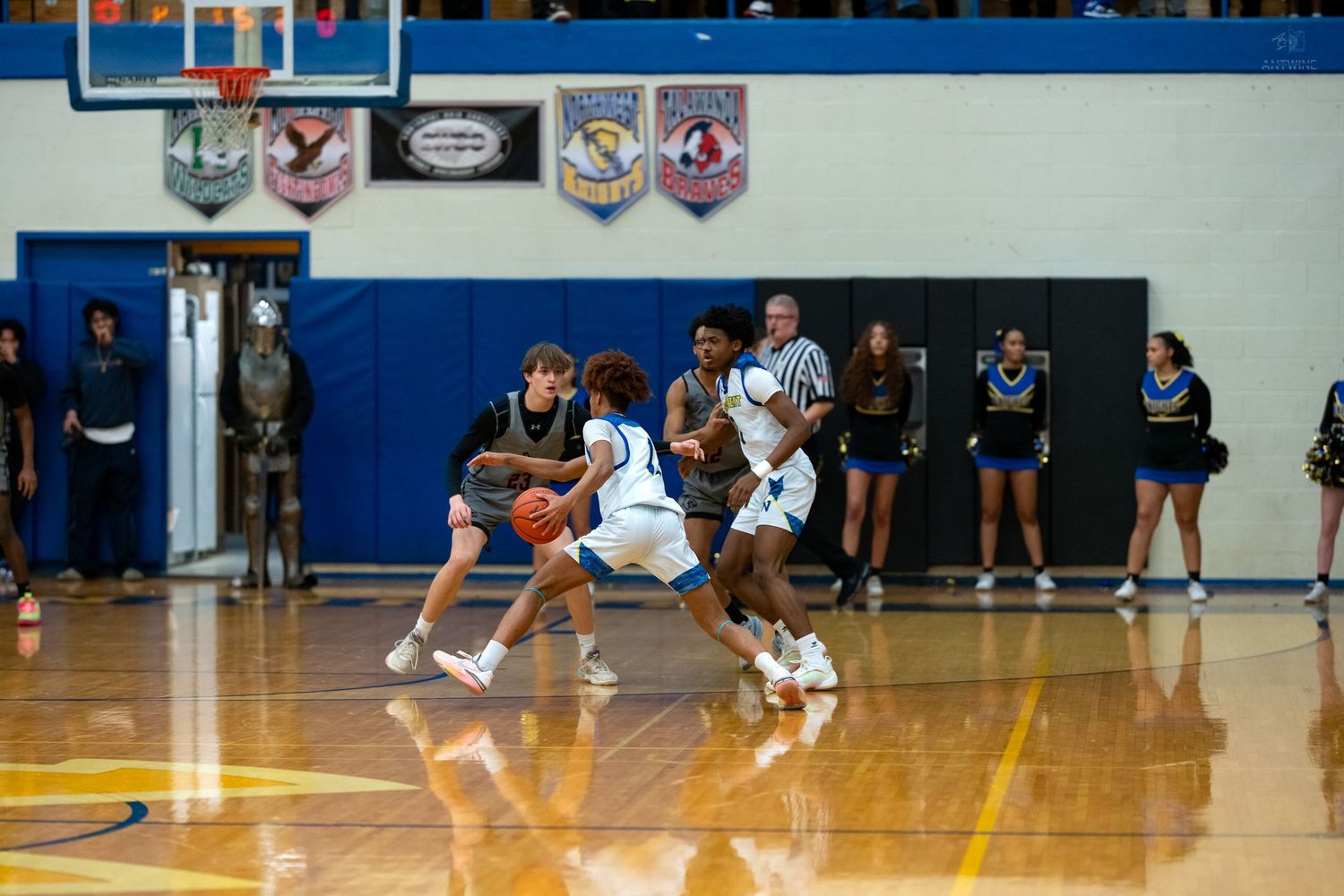 Two high school basketball players compete in a defensive matchup on a polished indoor gymnasium court.