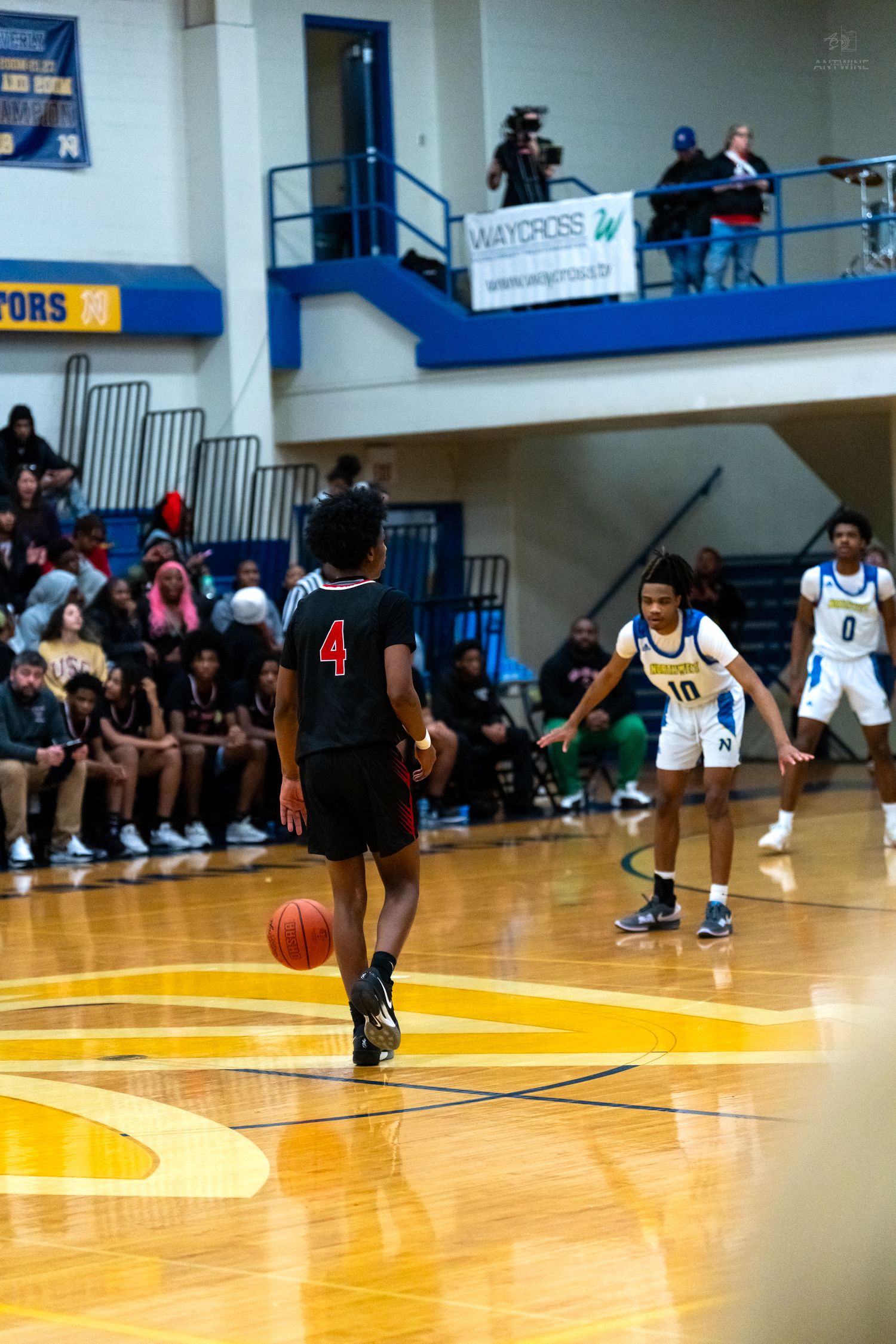 Player number 4 in black uniform dribbles upcourt while blue and white team defenders position in background.