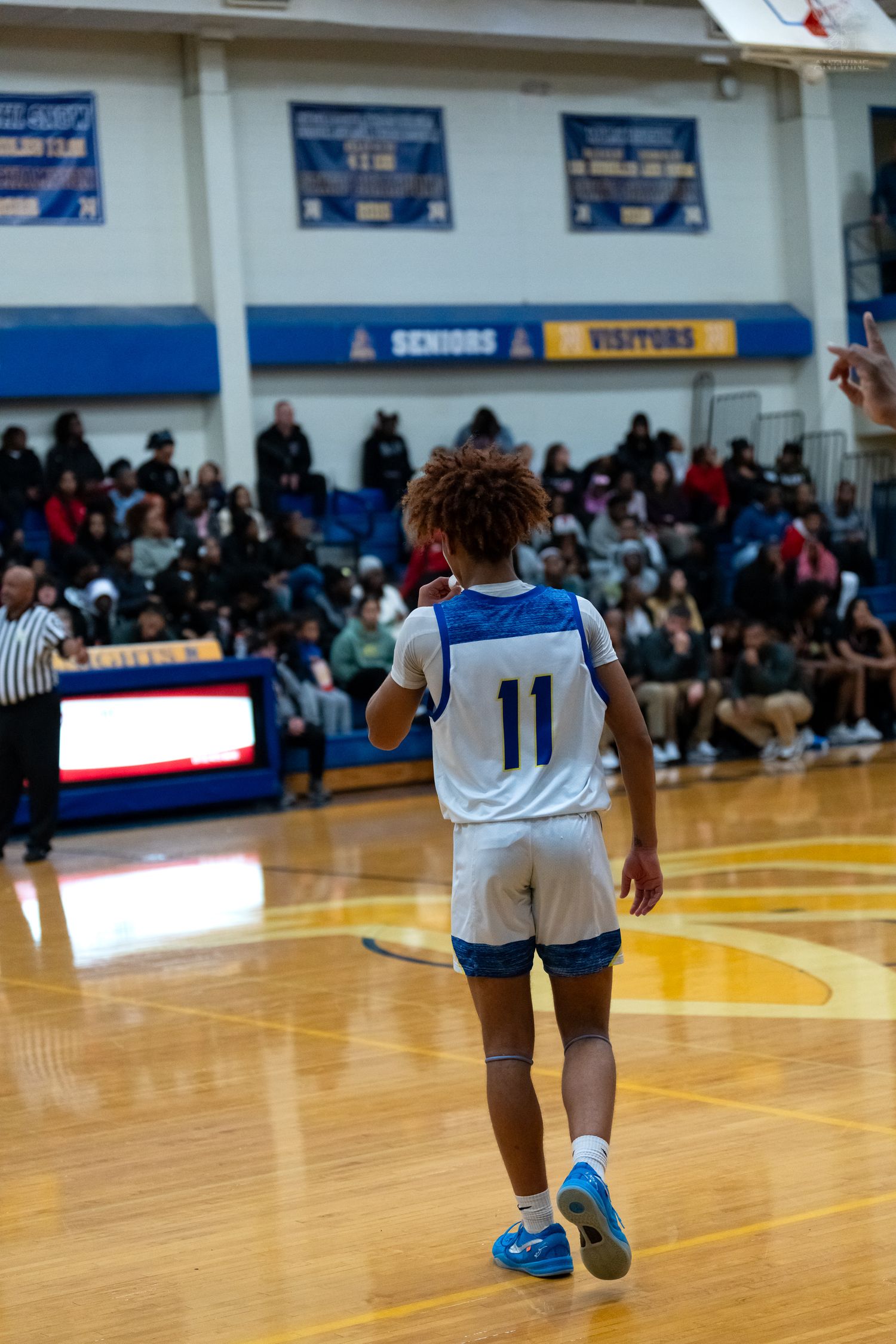 Player #11 in blue uniform signals during high school basketball game.