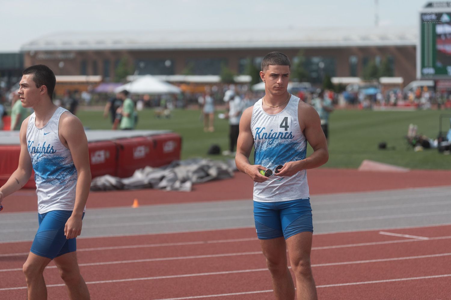 Two male track athletes in Knights uniforms prepare for a race at an outdoor track and field competition.