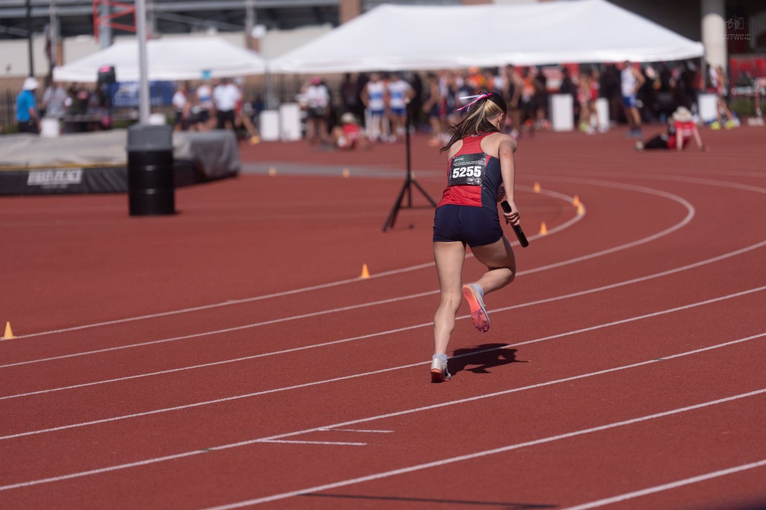 A female runner with a prosthetic leg competes on a red track at an outdoor track and field event.
