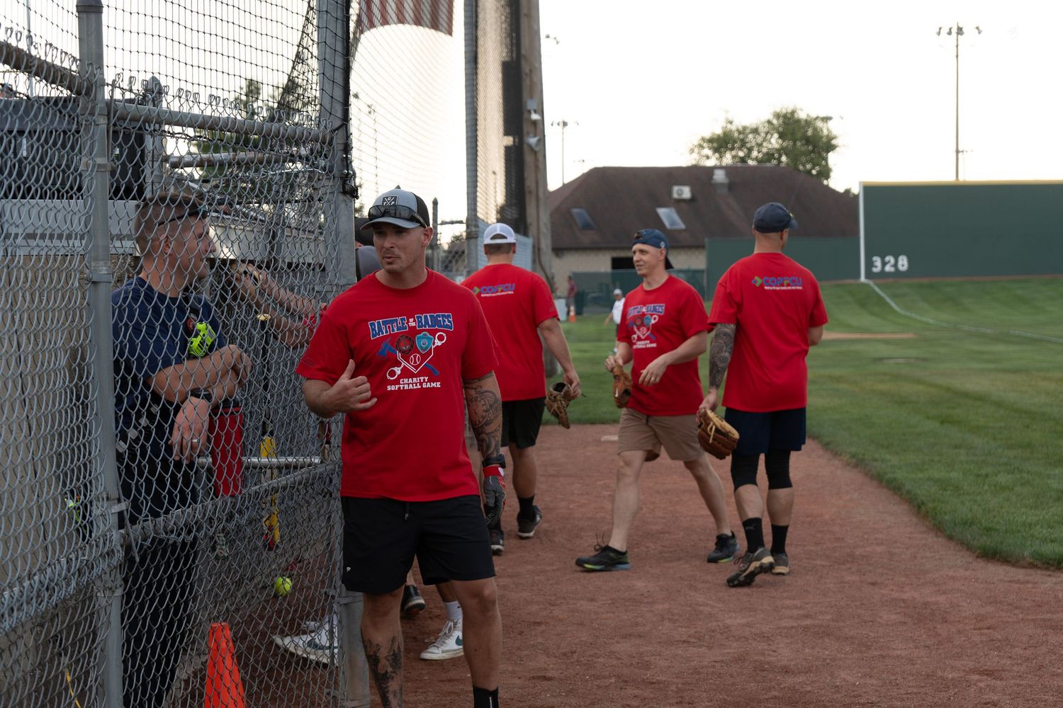 Group of adults in red t-shirts playing softball on an outdoor baseball field during a community sports event.