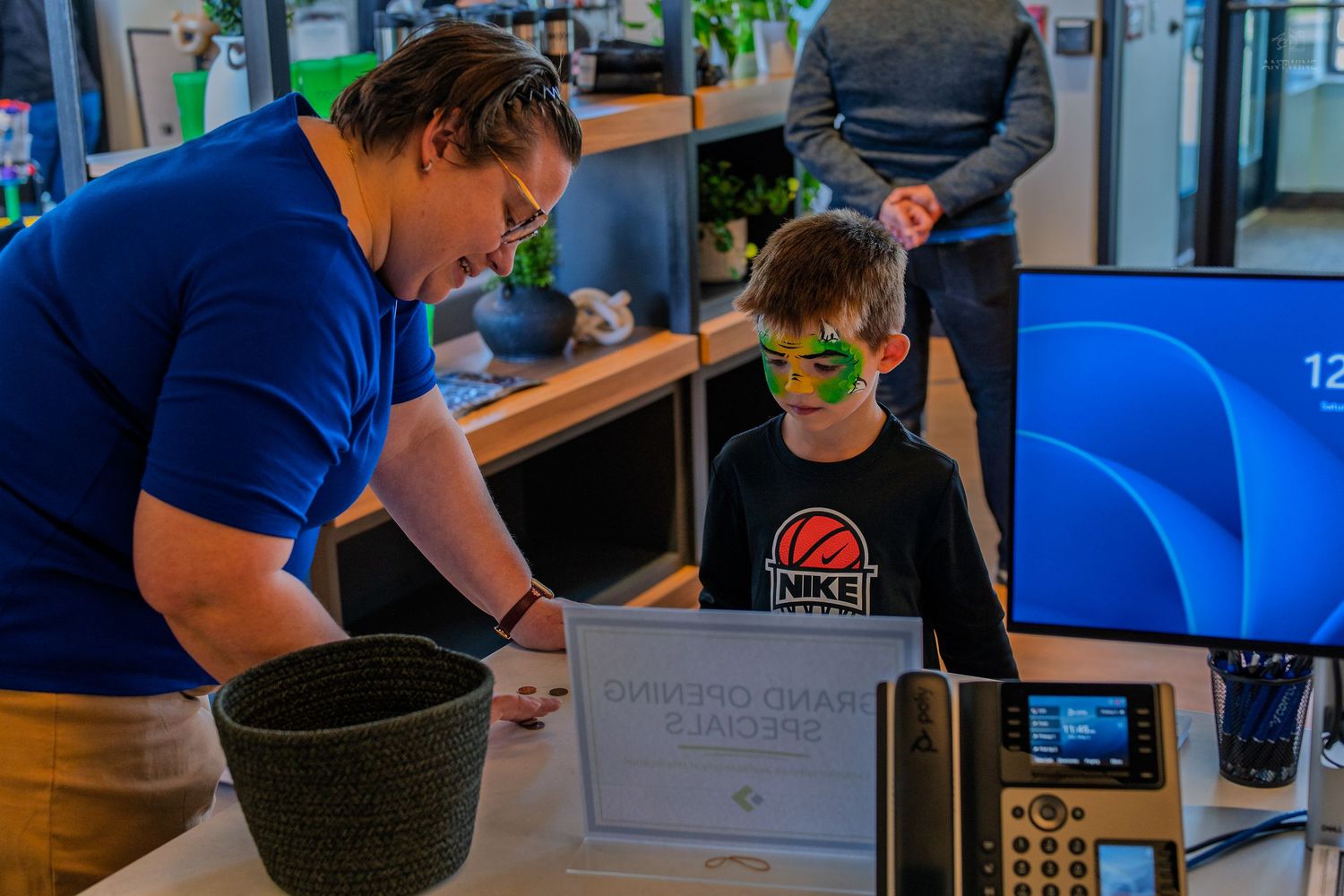 Child with green face paint checks in at a desk with an adult at a fun kids event.