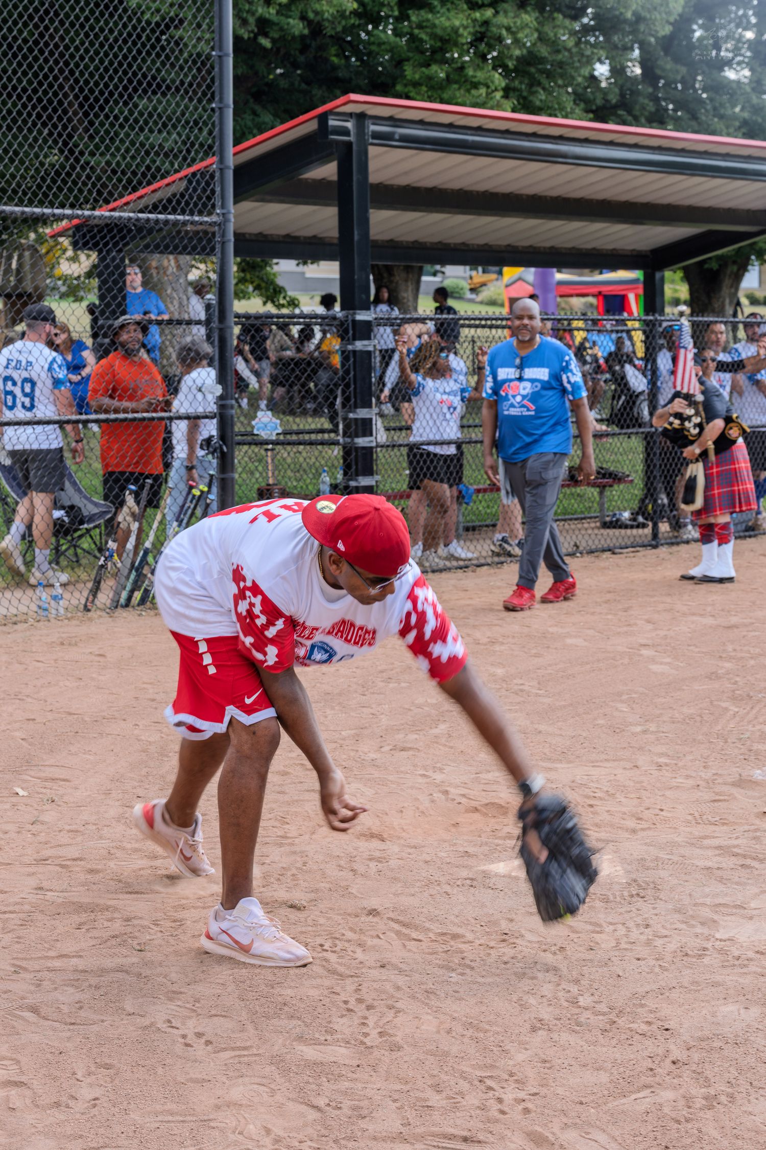 A baseball player in red and white uniform fields a ball with a glove on a dirt diamond during a recreational game.