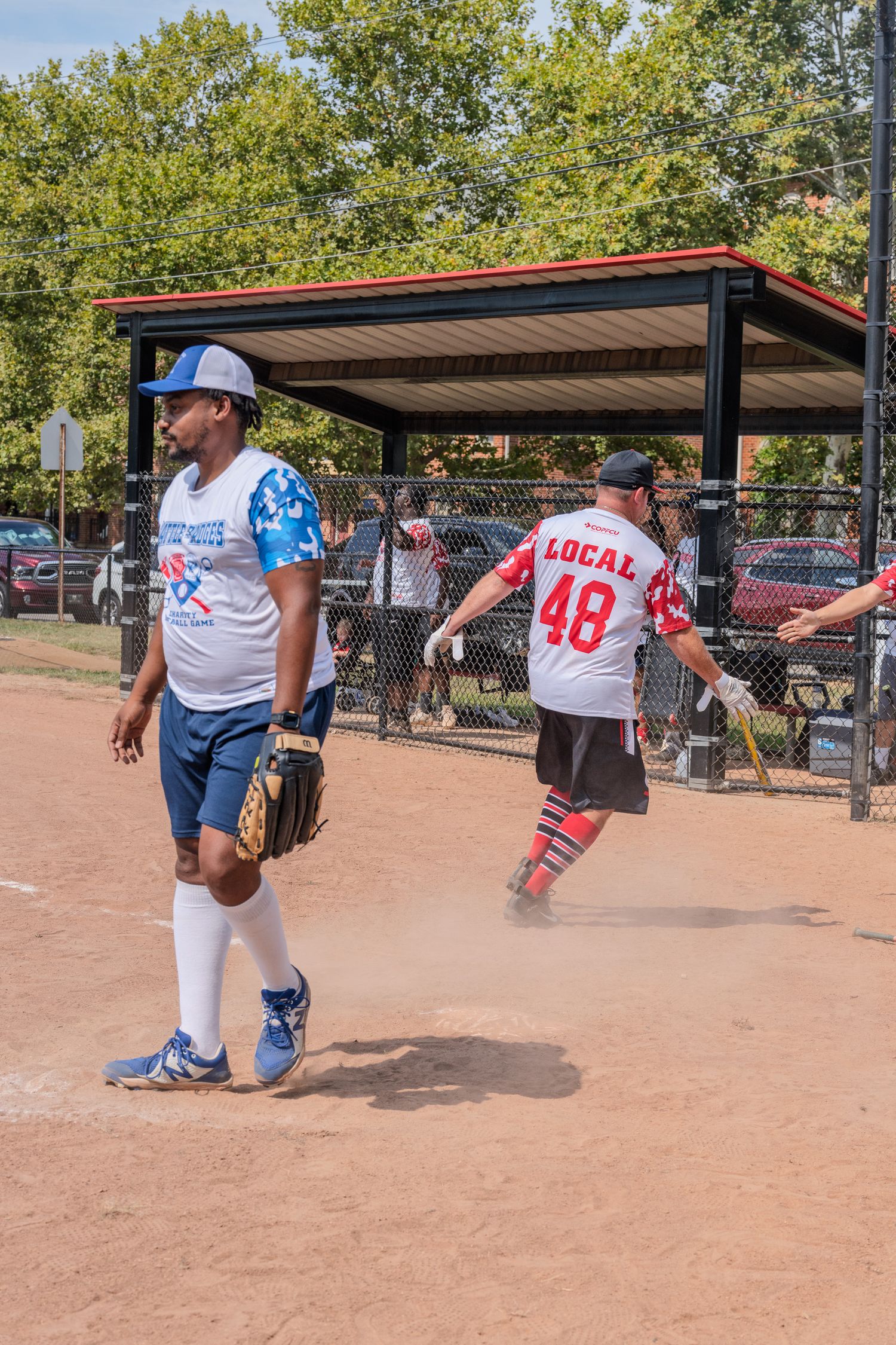 Softball players near dugout with player wearing Local 48 jersey kicking up dirt.