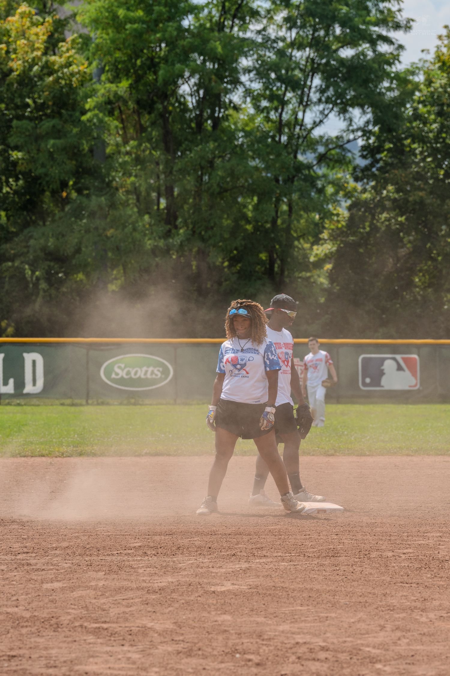 Female softball player stands on second base in a dust cloud with a teammate nearby on the field.