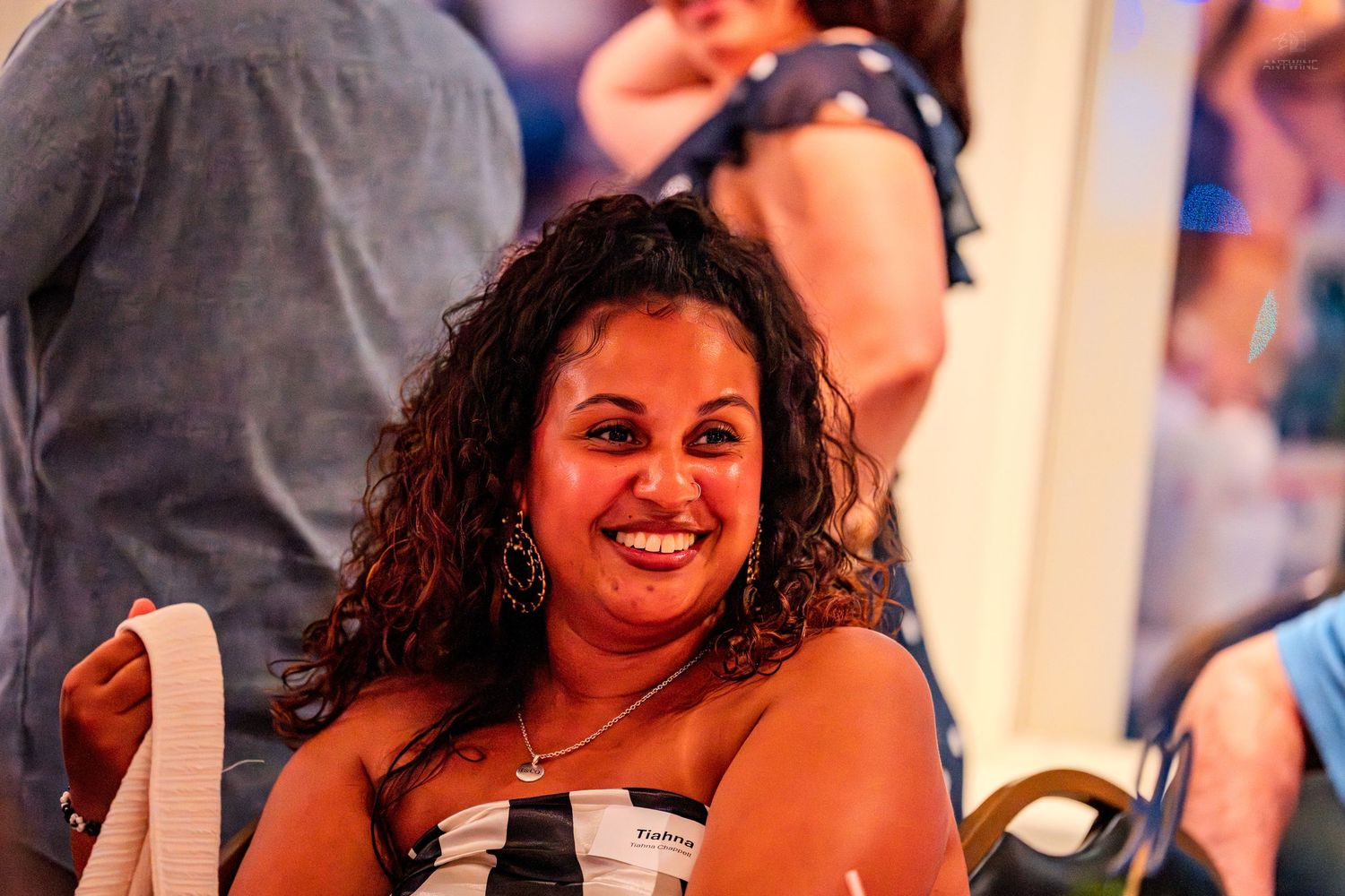 A smiling woman with curly hair enjoys a festive event wearing a striped top.