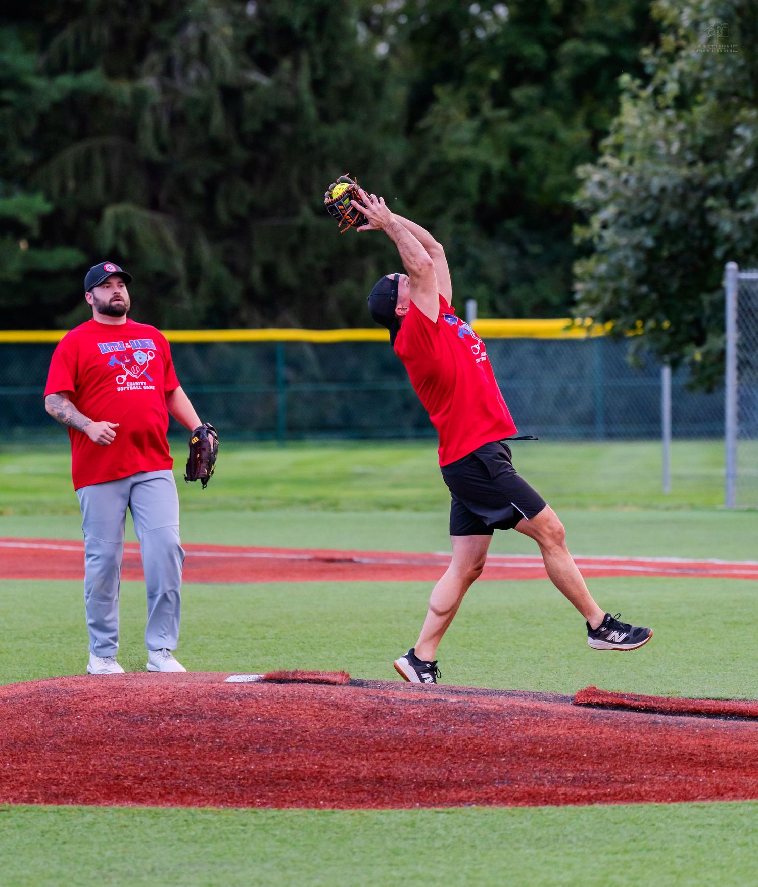 Red team softball player leaping to catch a ball while teammate watches during a recreational game.