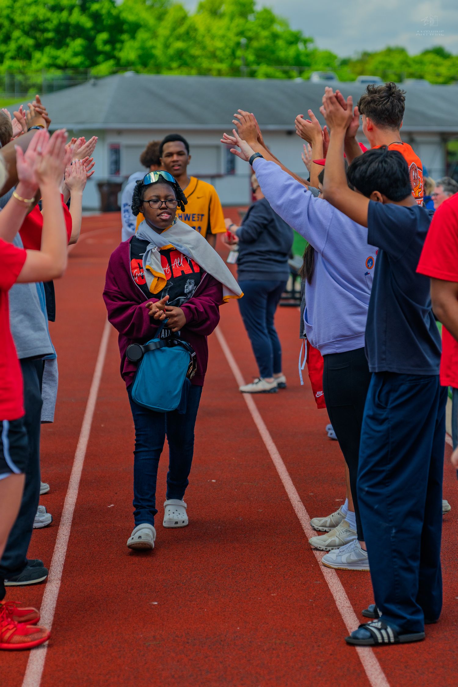 Athletes walk through a cheering tunnel of supporters on a red track during a Special Olympics event outdoors.