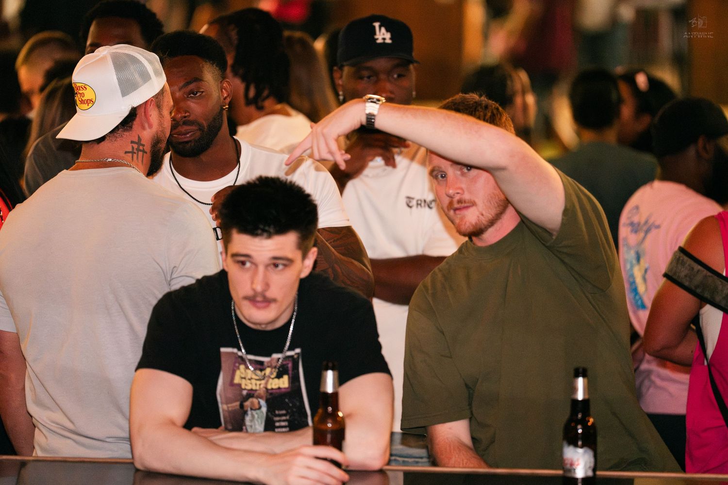 Two men sitting at a bar looking relaxed amid a busy crowd at a nightclub event.