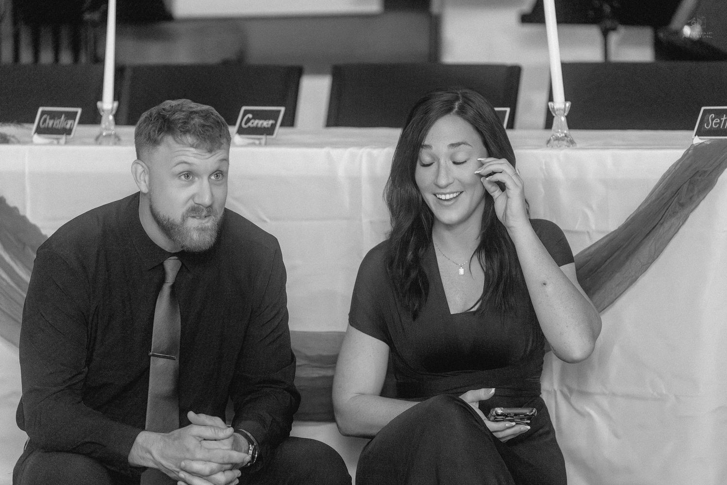 Black and white photo of a man in a tie and woman in black dress sitting together at an elegant event.