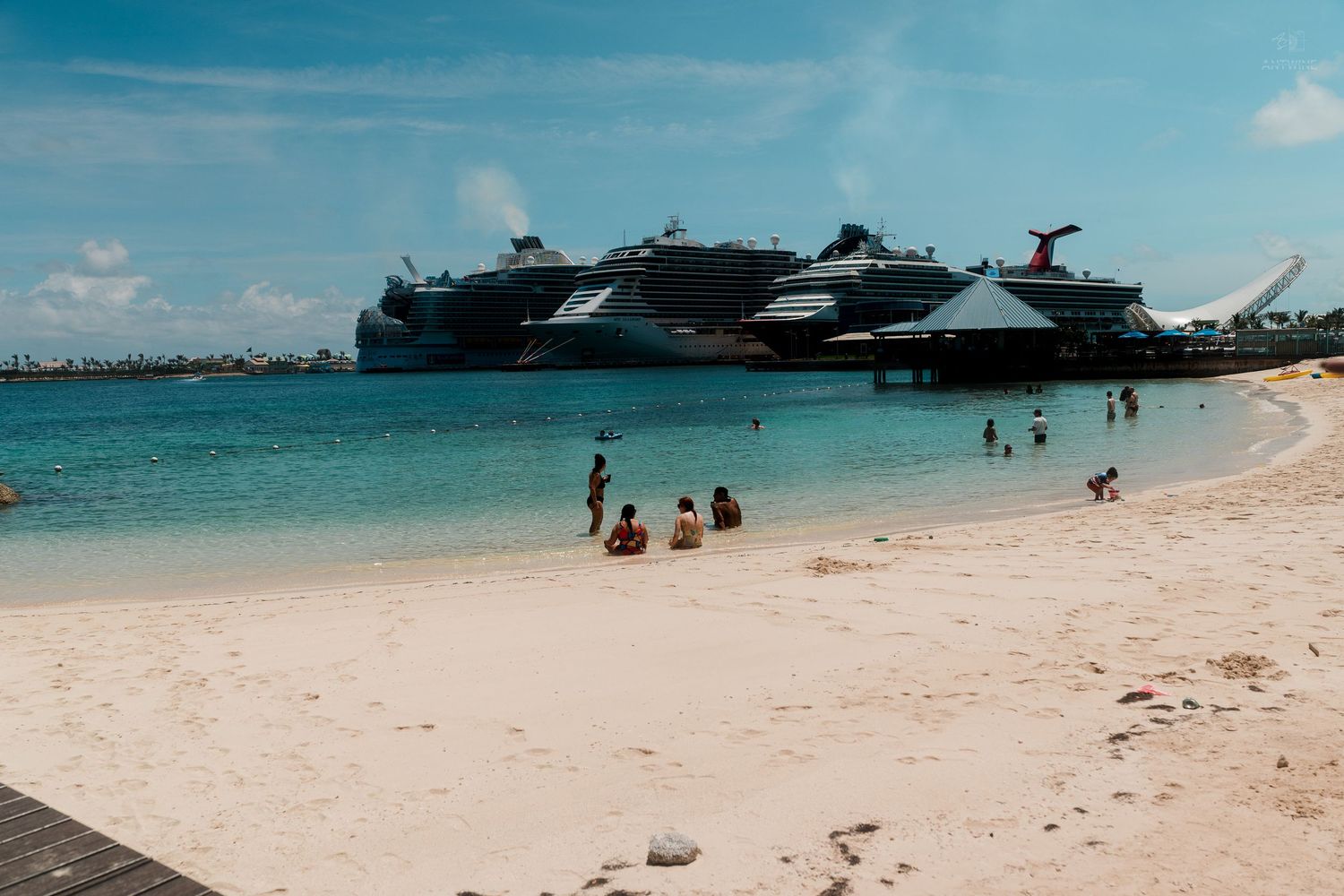 Sandy beach with swimmers and large cruise ships docked at a Caribbean port in the background.