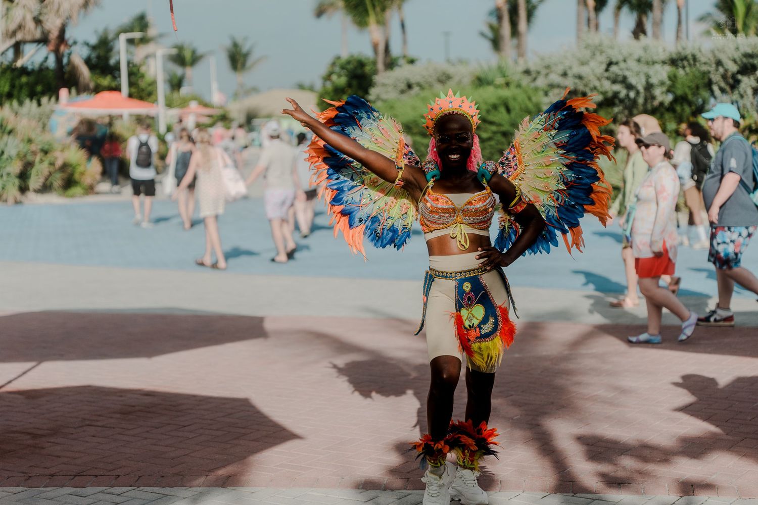 A performer in vibrant colorful feathered costume entertains tourists at a tropical destination.