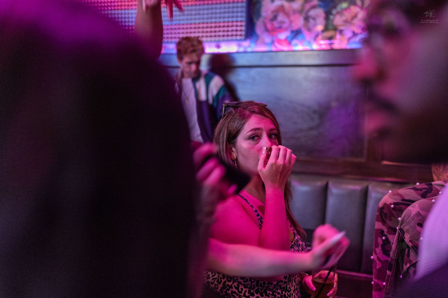 Woman drinking at a crowded nightclub bathed in pink neon lighting.