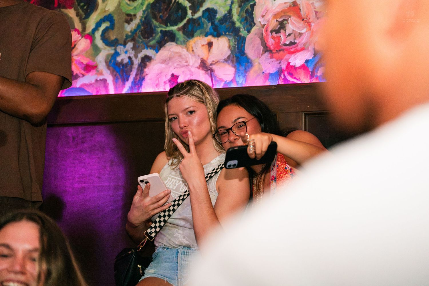 Two young women posing and pointing at a fun nightclub party with floral decor.