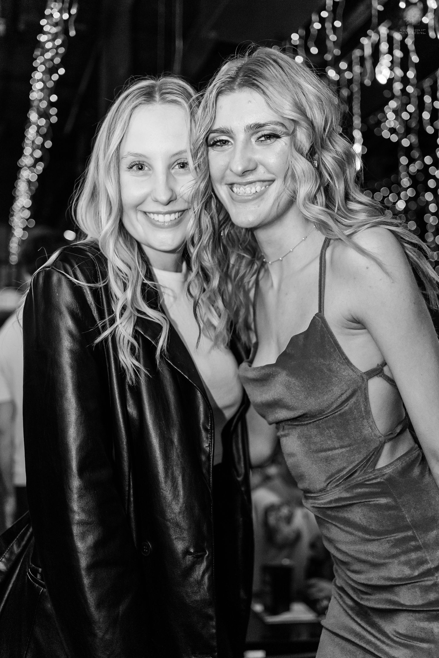 Two smiling women posing together at a festive venue with bokeh lights in the background.